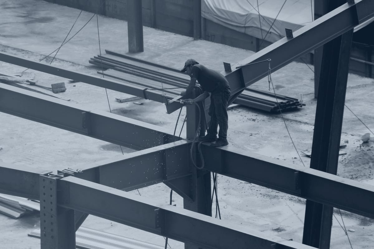 Steel worker cutting a structural member with a torch, sparks trailing.
