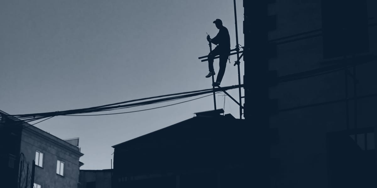 Ironworker silhouette moving along a steel beam against the sky.