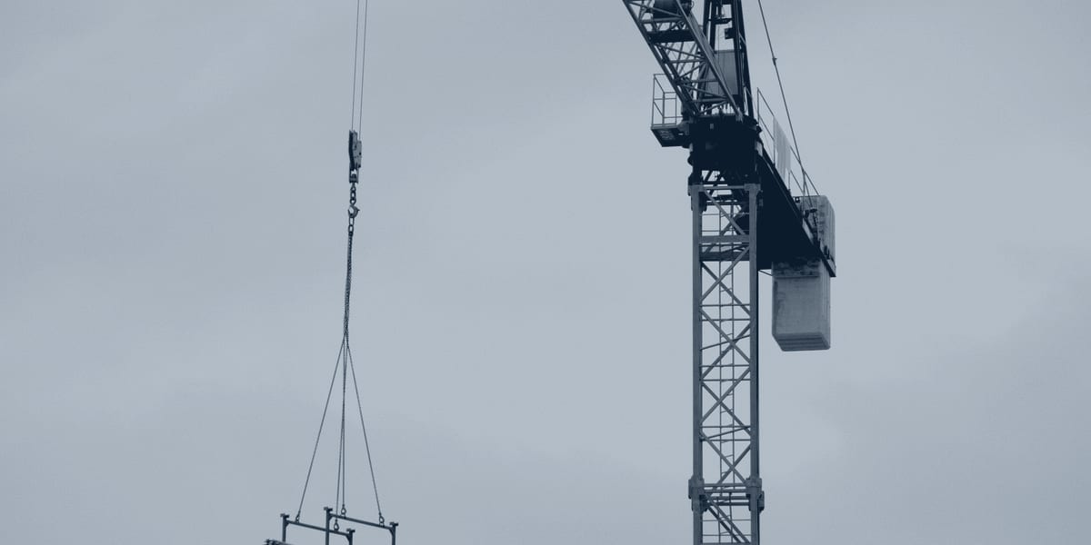 Crane hoisting a steel beam into place against an open sky during erection.